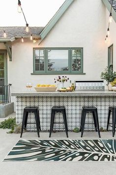 an outdoor bar with three stools in front of it and lights hanging from the ceiling