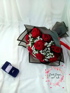 a bouquet of red roses and baby's breath on a white sheet next to a cell phone