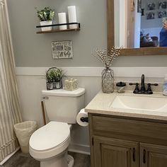 a white toilet sitting next to a sink in a bathroom under a mirror and wooden cabinets