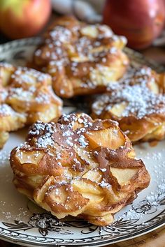 several pastries on a plate with powdered sugar and an apple in the background