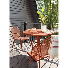 an orange table and two chairs on a deck with a potted plant in the corner