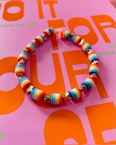 a colorful bracelet is sitting on top of a pink book with an orange and blue stripe design