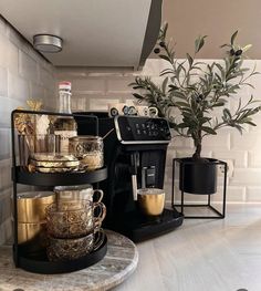 there is a coffee maker on the counter next to some cups and saucers in front of a potted plant