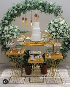 a table topped with cakes and cupcakes under a wedding cake arch covered in greenery