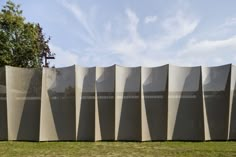 a wall made out of metal mesh sitting on top of a grass covered field next to a tree