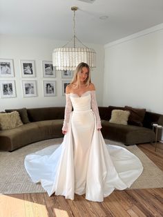 a woman in a white wedding dress standing on the floor with her arms behind her back