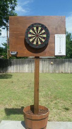 a wooden sign with a dart on it in the middle of a yard next to a potted plant