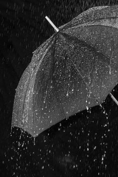 black and white photograph of an umbrella in the rain with water splashing on it