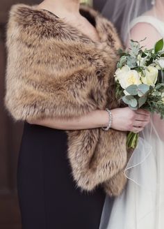 the bride is holding her bouquet in her hand and she is wearing a fur stole