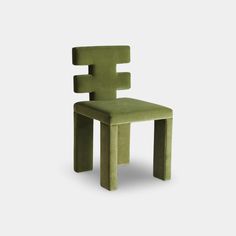 a green chair sitting on top of a white floor next to a gray wall with an odd shaped seat