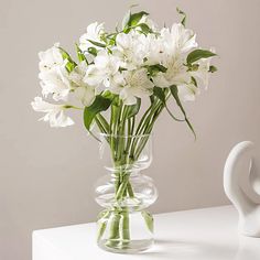 white flowers are in a clear vase on a table