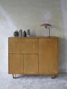 a wooden cabinet with three bottles on top and a lamp next to it, against a white wall