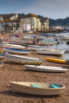 many small boats are lined up on the shore by the water's edge, with houses in the background