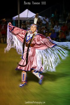 a woman dressed in pink and white is dancing with feathers on her head while people watch from the stands