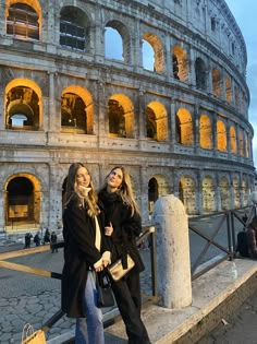 two women standing next to each other in front of the colossion, rome