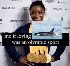 a woman holding two gold olympic medals in front of a poster with an orca on it