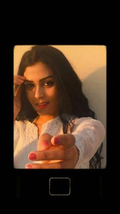 a woman with long dark hair pointing her finger at the camera while wearing a white shirt