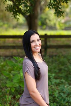 a woman standing in front of a tree with her hands on her hips and smiling at the camera