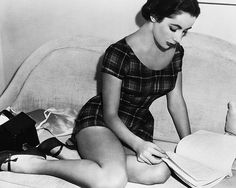 a woman sitting on a couch reading a book with her legs crossed and wearing high heels