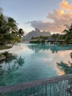 an outdoor swimming pool surrounded by palm trees and mountains in the distance with water running through it