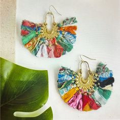 two pairs of colorful earrings on top of a white table next to a green plant