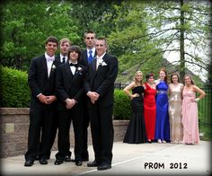 a group of young men and women in formal wear posing for a photo on the sidewalk