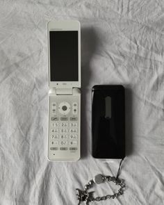 an old cell phone is next to a new one on a bed with a chain