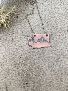 A piece of copper is impressed with a mountain range design and cut into the shape of Washington State. Perfect necklace to show your home state love! Has a brushed finish and given a darkened oxidized finish. Washington measures 1 inch wide and 5/8 inch tall. Hangs from an 18 in stainless steel cable chain with trigger clasp. 16 or 20 inch can be requested at checkout. Range Design, Beach Cove, Stainless Steel Cable, Mountain Range, Washington State, Cable Chain, Dog Tag Necklace, 1 Inch, Washington