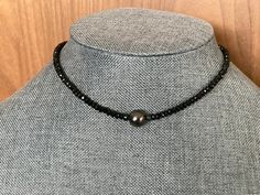 This black on black choker is a true showstopper. I've chosen one beautiful 9mm Tahitian black pearl, AAA/AA quality, and paired it with 4mm black Tourmaline faceted rondelles to make a choker that is a black lover's dream.  The Tahitian pearl is a genuine South Sea pearl imported from Tahiti and has not been dyed or colored in any way. The pearl is truly the center of attention in this piece but the inky opaque sparkling faceted black schorl Tourmaline rondelles aren't exactly wallflowers.  The pearl is very subtly set off from the opals by two tourmaline stones that, when lit from behind, show they are actually more blue green to hint at the green and blue luster in the pearl they flank.  I have a few sizing options; please measure your neck with a string and then measure the string with Black Single Strand Pearl Necklace, Formal Black Tahitian Pearl Necklace, Formal Black Tahitian Pearl Jewelry, Black Tahitian Pearl Round Beads Jewelry, Black Tahitian Pearl Jewelry With Round Beads, Black Tahitian Pearl Necklace With Pendant, Formal Black Jewelry With Pearl Pendant, Formal Black Pearl Pendant Jewelry, Formal Black Tahitian Pearl Necklaces