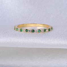 an emerald and diamond wedding band on a white cloth with the ring resting on it's side