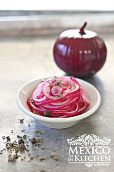 a bowl filled with sliced red onions next to an onion on top of a table