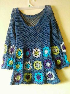 a blue crocheted sweater hanging on a white hanger next to a wall