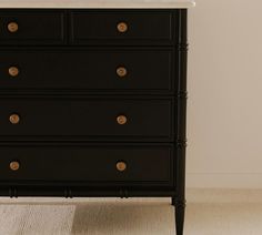 a black dresser with white marble top and brass knobs on the drawers, in front of a beige wall