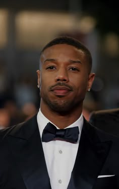 a close up of a person wearing a tuxedo and bow tie with other people in the background