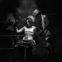 a woman sitting on top of a chair next to two men in a boxing ring