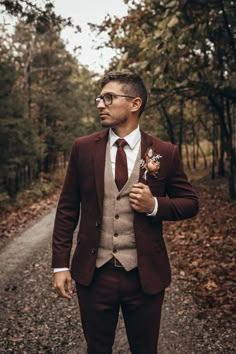 a man in a suit and tie standing on a path with trees behind him wearing glasses