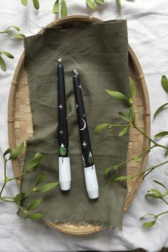 two black and white pens sitting on top of a green cloth next to some leaves