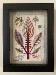 an art piece with feathers and beads in a black frame