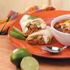 two burritos on an orange plate with a bowl of chili and lime next to it