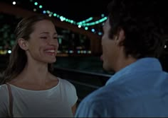 a man and woman standing next to each other in front of a city at night