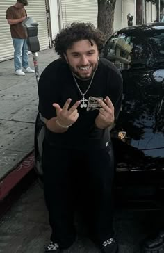 a man standing next to a black car on the side of a road with his hands in the air