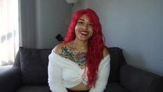 a woman with red hair is sitting on a couch and smiling at the camera while wearing a white shirt