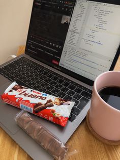 a laptop computer sitting on top of a wooden desk next to a cup of coffee