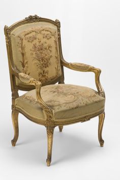 an antique chair with floral fabric and gold trimmings on the back, sitting in front of a white background