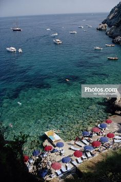 the beach is crowded with umbrellas and boats in the water near some rocky cliffs