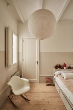 a bedroom with a bed, chair and lamp hanging from the ceiling in front of a door