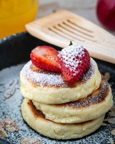 a stack of pancakes covered in powdered sugar with a strawberry on top