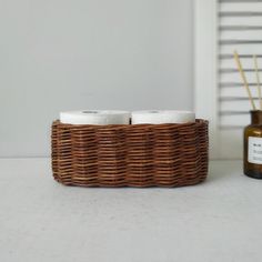 two rolls of toilet paper sitting in a wicker basket next to an empty bottle