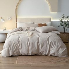 a bed with white sheets and pillows on top of it in a room next to a potted plant