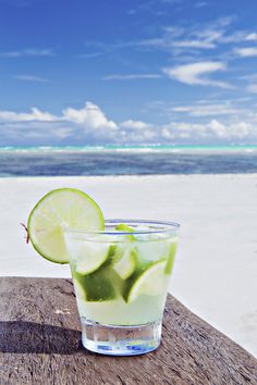 a glass filled with limeade sitting on top of a wooden table next to the ocean